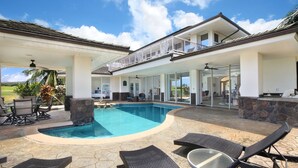 Una casa de dos pisos con piscina, mobiliario exterior y un balcón.