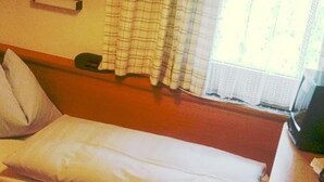 A single bed with a pillow, a bedside table, and a window with curtains.