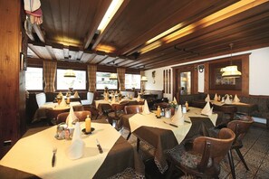 Un restaurant avec des poutres en bois, des tables décorées de bougies et une vue sur l’extérieur.