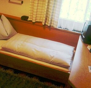 Un lit simple avec un oreiller, une table de chevet et une fenêtre avec des rideaux.