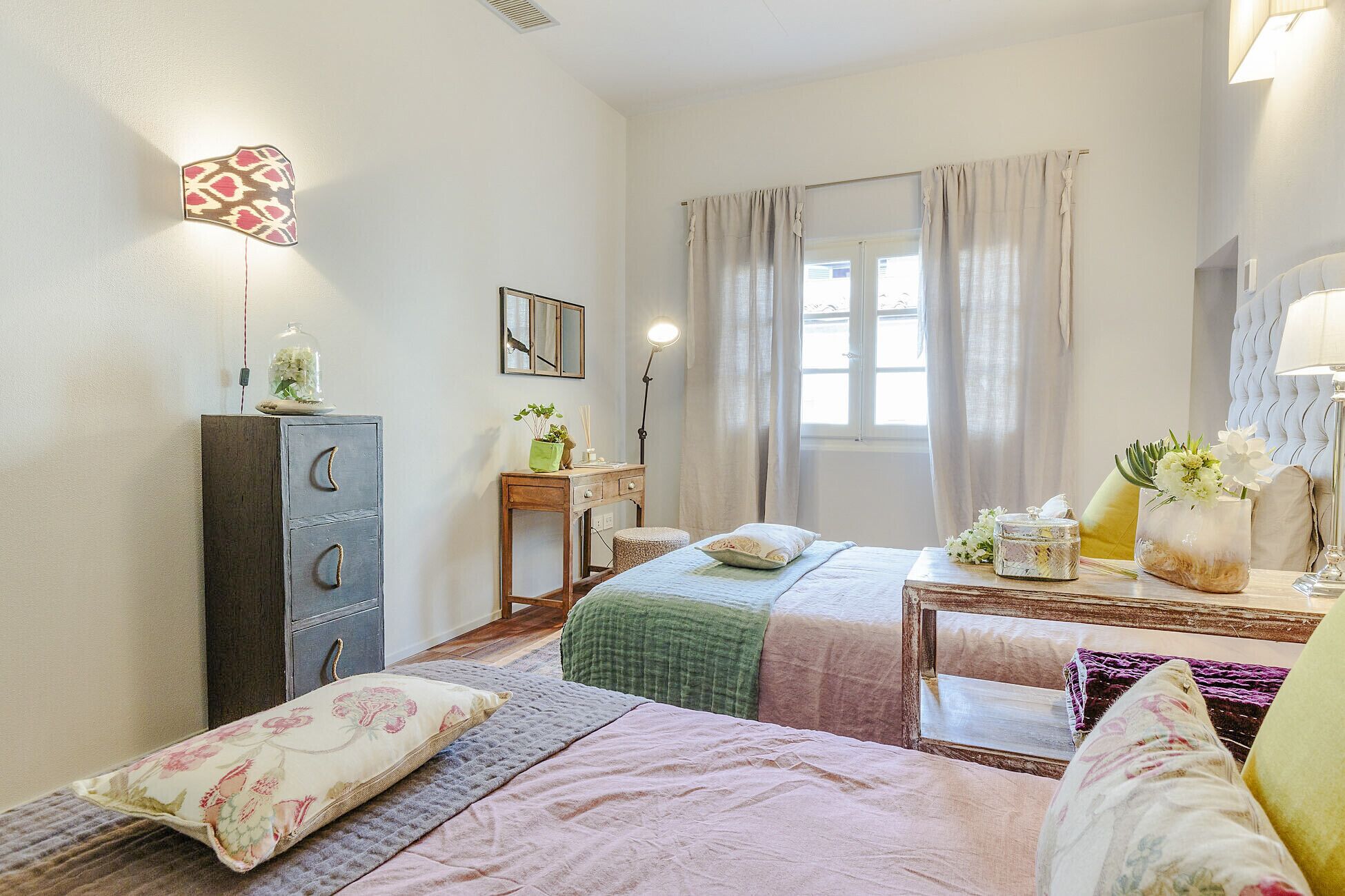 Une chambre à coucher avec un lit, des tables de chevet, une commode, un miroir et une fenêtre avec des rideaux.