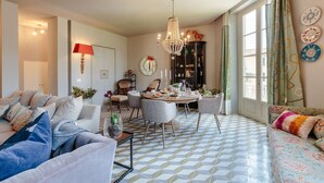 Un comedor con candelabro, una mesa redonda y sillas. Hay un sofá y un aparador con platos decorativos en la pared.
