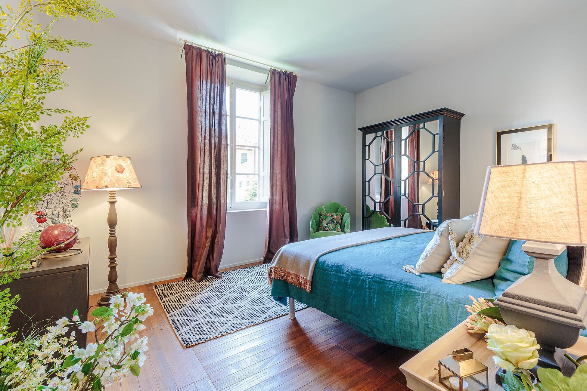 A bedroom with a bed, a window with curtains, a lamp, and a decorative wall piece.