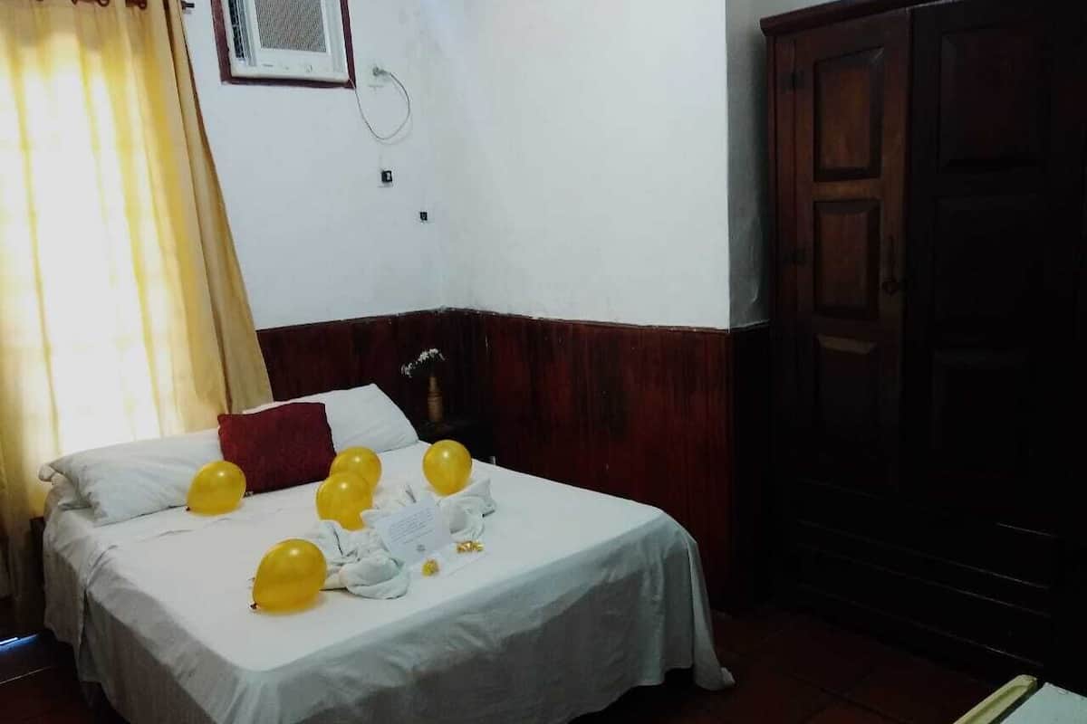 A hotel room with a bed, yellow balloons, a red pillow, and a wooden wardrobe.
