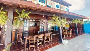 An outdoor dining area with wooden tables and chairs, potted plants, and a brick wall. - Pousada Tartaruga (Rio das Ostras)