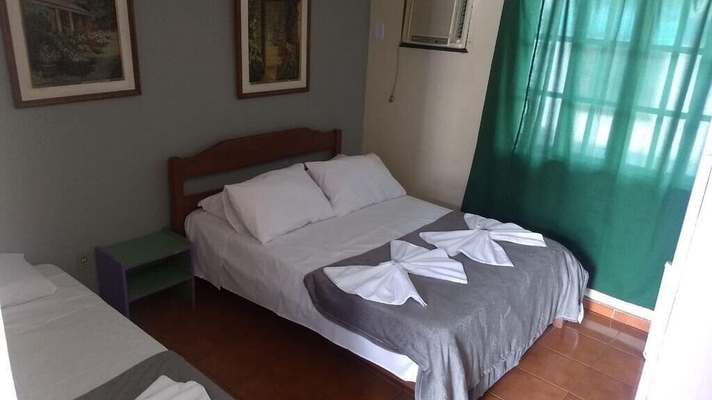 A hotel room with a single bed, a nightstand, and a window with green curtains.