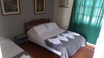 Una habitación de hotel con una cama individual, una mesita de noche y una ventana con cortinas verdes.