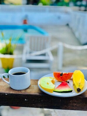 A wooden deck with a white chair, a plate of fruit, and a cup of coffee. - Pousada Tartaruga (Rio das Ostras)