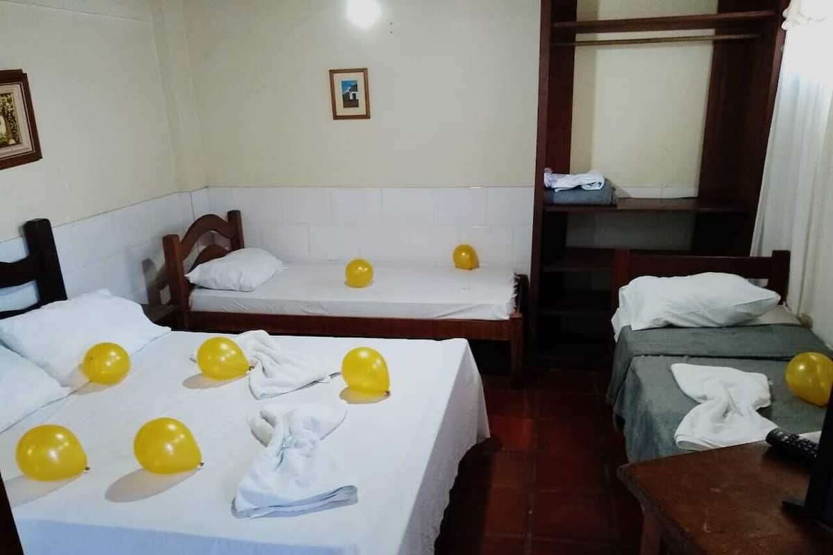 A hotel room with two single beds, a bunk bed, and a small table with a remote control.