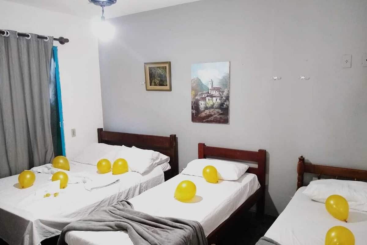 A hotel room with three single beds, each with a white bedspread and a pair of yellow balloons.