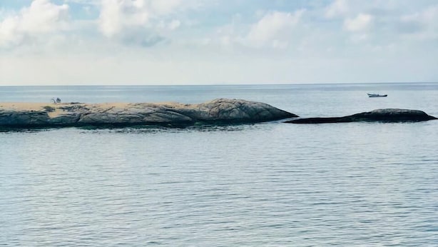 A hand holding a white mug with a beverage, overlooking a beach with calm waters and distant rocks. - Pousada Tartaruga (Rio das Ostras)