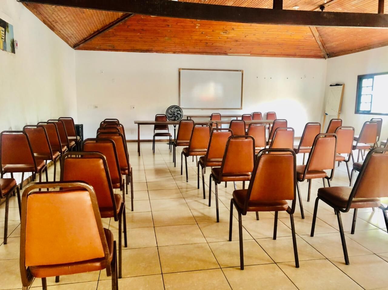 Una sala de conferències amb files de cadires marrons, una pissarra i un sostre de fusta.