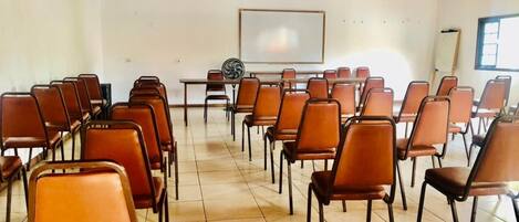 Un salón de conferencias con hileras de sillas marrones, una pizarra y techo de madera.