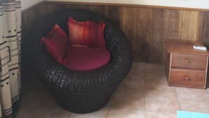 Une pièce avec un fauteuil en osier, une petite table de chevet en bois et un climatiseur fixé au mur.