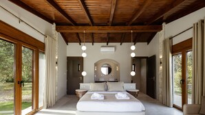 Een ruime slaapkamer met een groot bed, houten balken in het plafond en grote ramen met uitzicht op de omgeving.