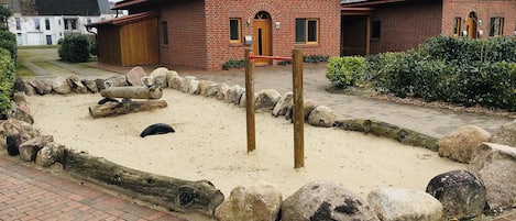 A brick building with a stone pathway, a wooden post, and a sandbox area.