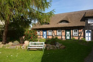 A traditional building with a thatched roof, a bench, and a garden with rocks and flowers. - B - Uns Schün, Germany (Middelhagen)