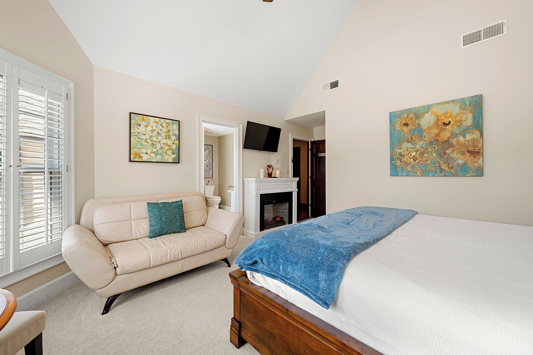 A bedroom with a bed, a sofa, a fireplace, and artwork on the walls.