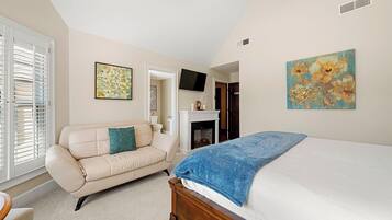 A bedroom with a bed, a sofa, a fireplace, and artwork on the walls.