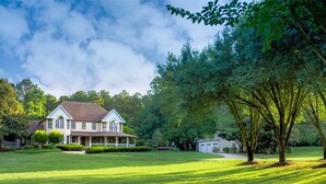 A large house with a porch, surrounded by a well-maintained lawn and trees.