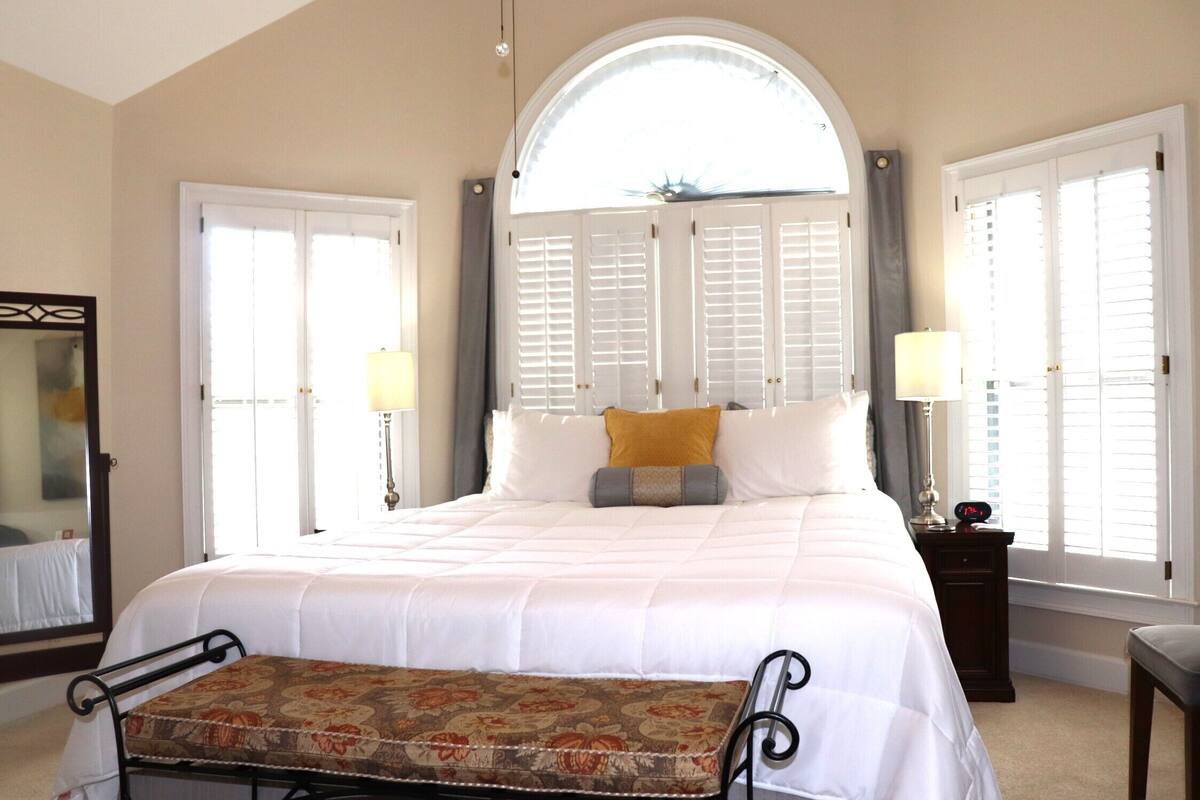 A bedroom with a large bed, two bedside lamps, a bench, and a mirror.