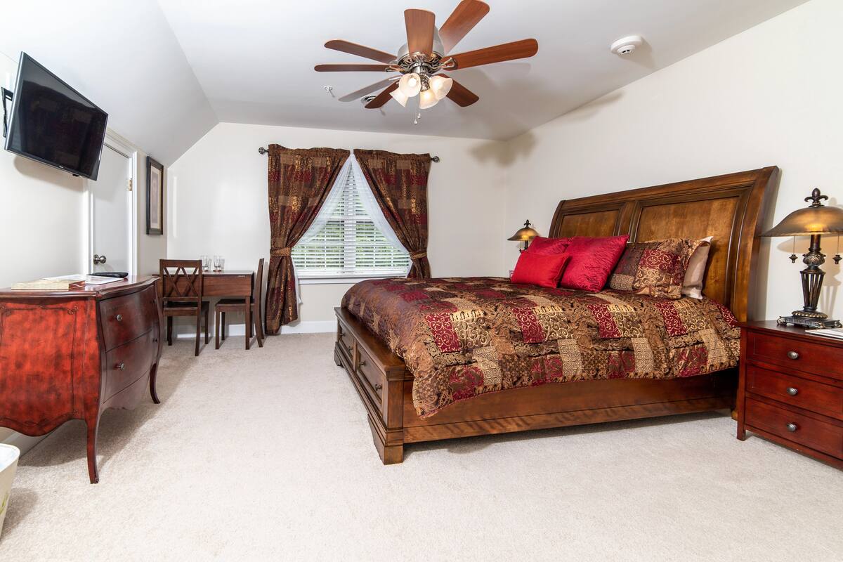 A bedroom with a wooden bed, a desk, a chair, a ceiling fan, and a window with curtains.