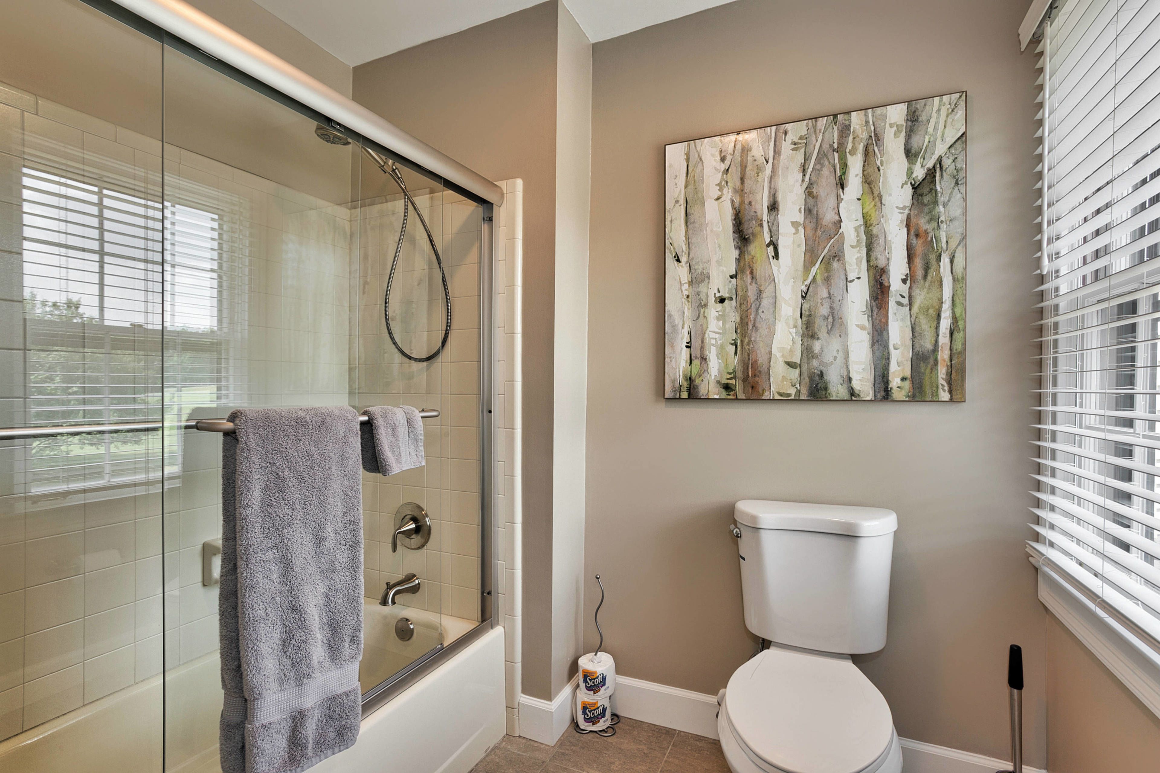 A bathroom with a glass-enclosed shower, a toilet, and a wall-mounted painting.