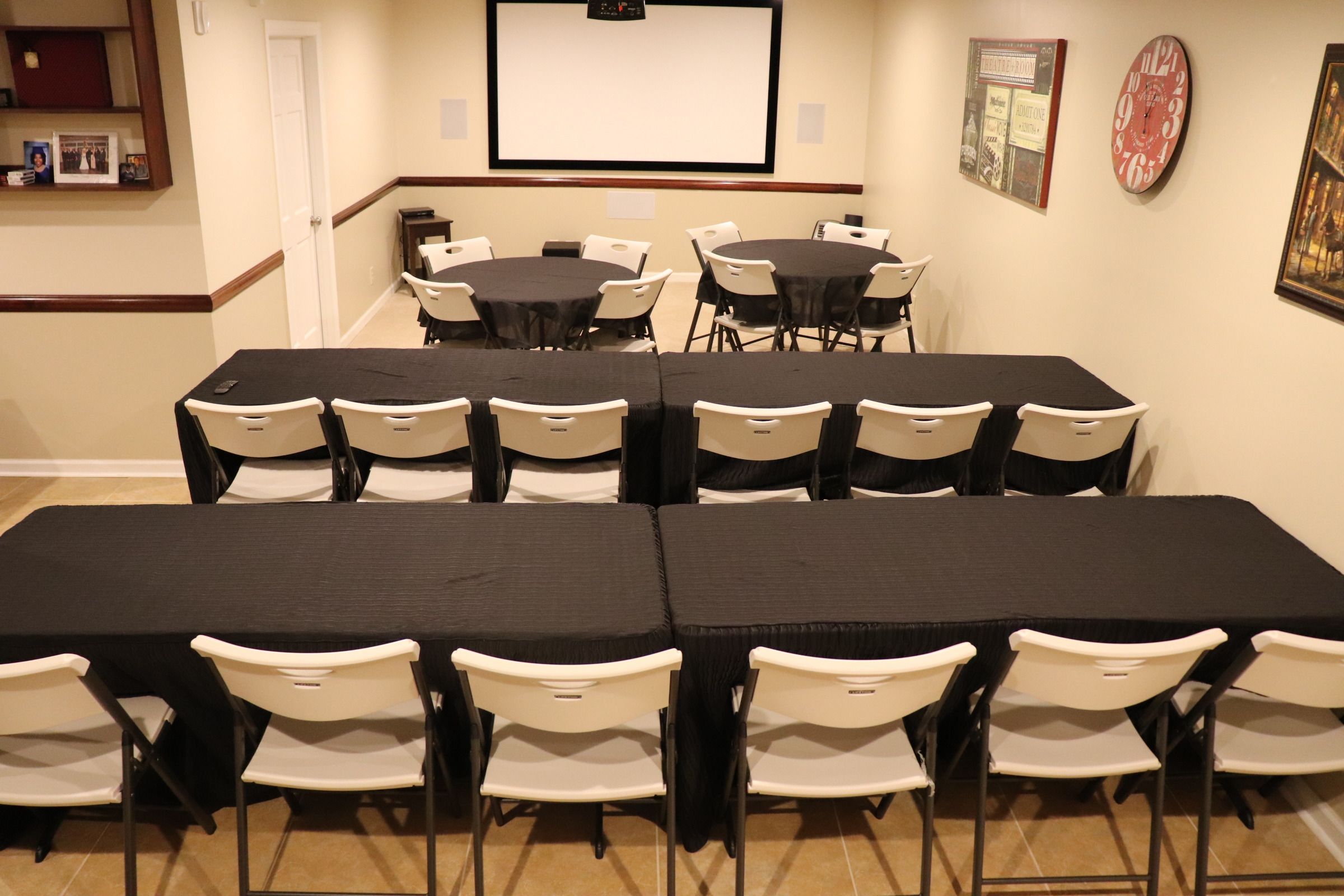 Un salón de conferencias con varias mesas y sillas, una pantalla de proyector y cuadros en las paredes.