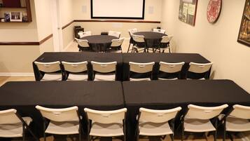 Un salón de conferencias con varias mesas y sillas, una pantalla de proyector y cuadros en las paredes.