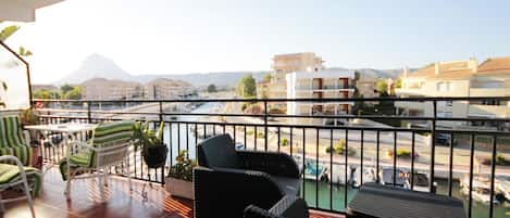 A balcony with wicker furniture, a view of a river, and buildings in the background.