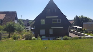 A two-story house with a sloped roof, a front porch, and a small garden area. - Central vacation apartment, barrier-free access, please contact us (Braunlage)