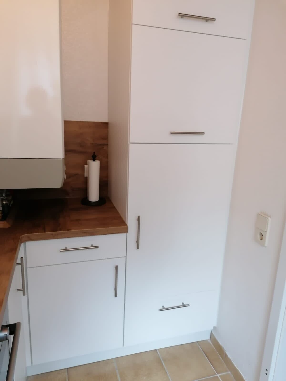 Une cuisine de taille réduite avec des meubles blancs, un plan de travail en bois et un évier blanc.