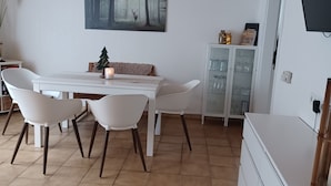 A dining area with a white table and chairs, a painting of a forest scene, a small Christmas tree, and a cabinet with glass doors. - Central vacation apartment, barrier-free access, please contact us (Braunlage)