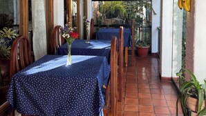 Eine überdachte Terrasse mit Tischen und Stühlen, einer hängenden Pflanze und Blick auf einen Garten.