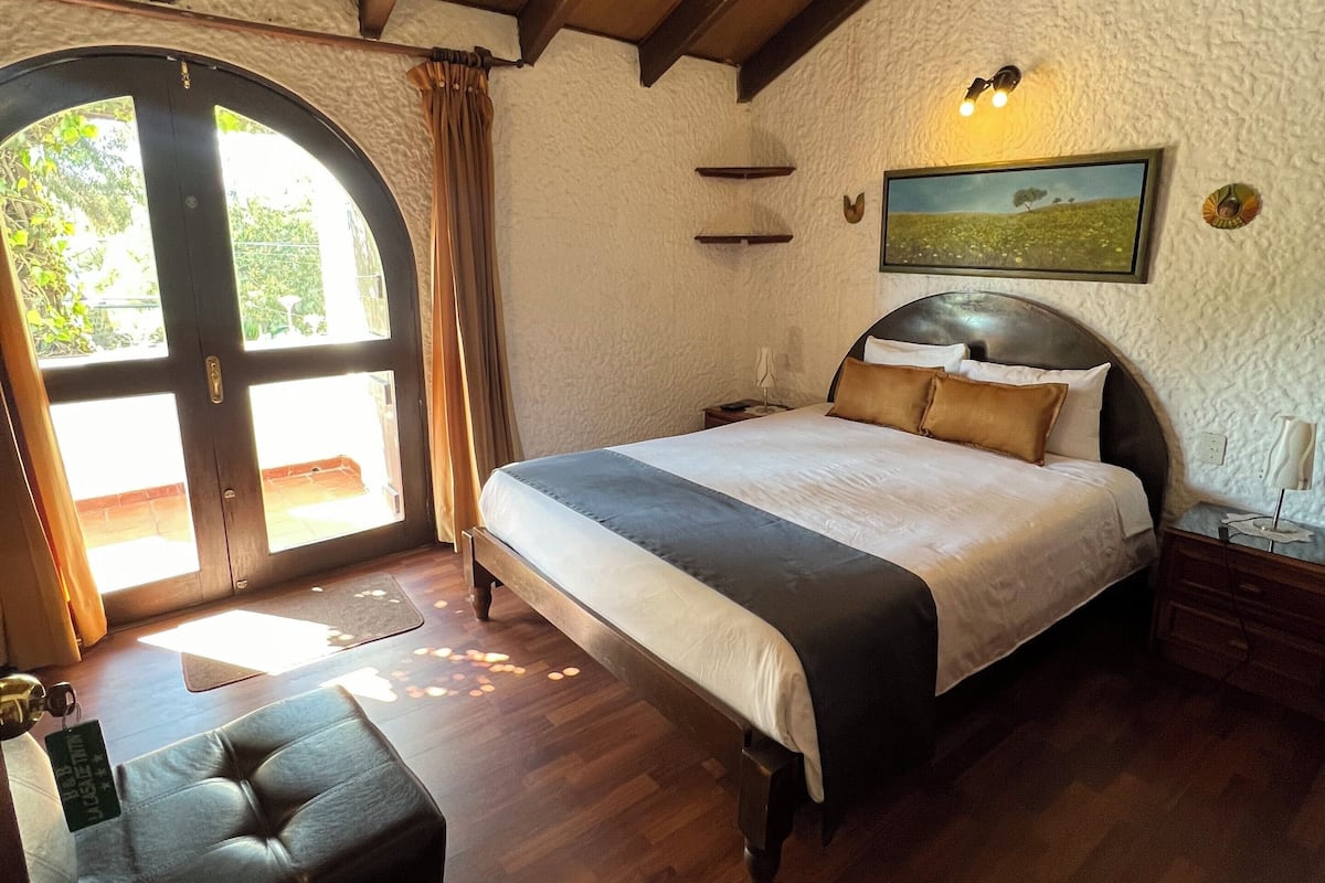 Un dormitorio con una cama grande, suelo de madera y vistas a través de una puerta.
