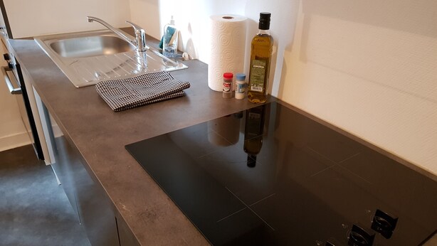 A modern kitchen with a stainless steel sink, a black induction cooktop, and a checkered placemat.