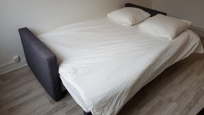 A single bed with a white mattress and pillows, a dark headboard, and a wooden floor.