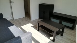 A room with a grey sofa, a small wooden table, a black cabinet, and a TV stand.