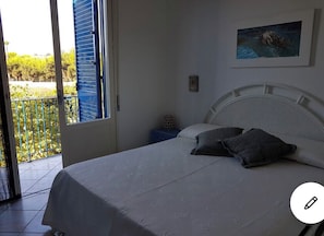 Relax in this serene bedroom with a large bed, white headboard, and a sliding door leading to an outdoor space.