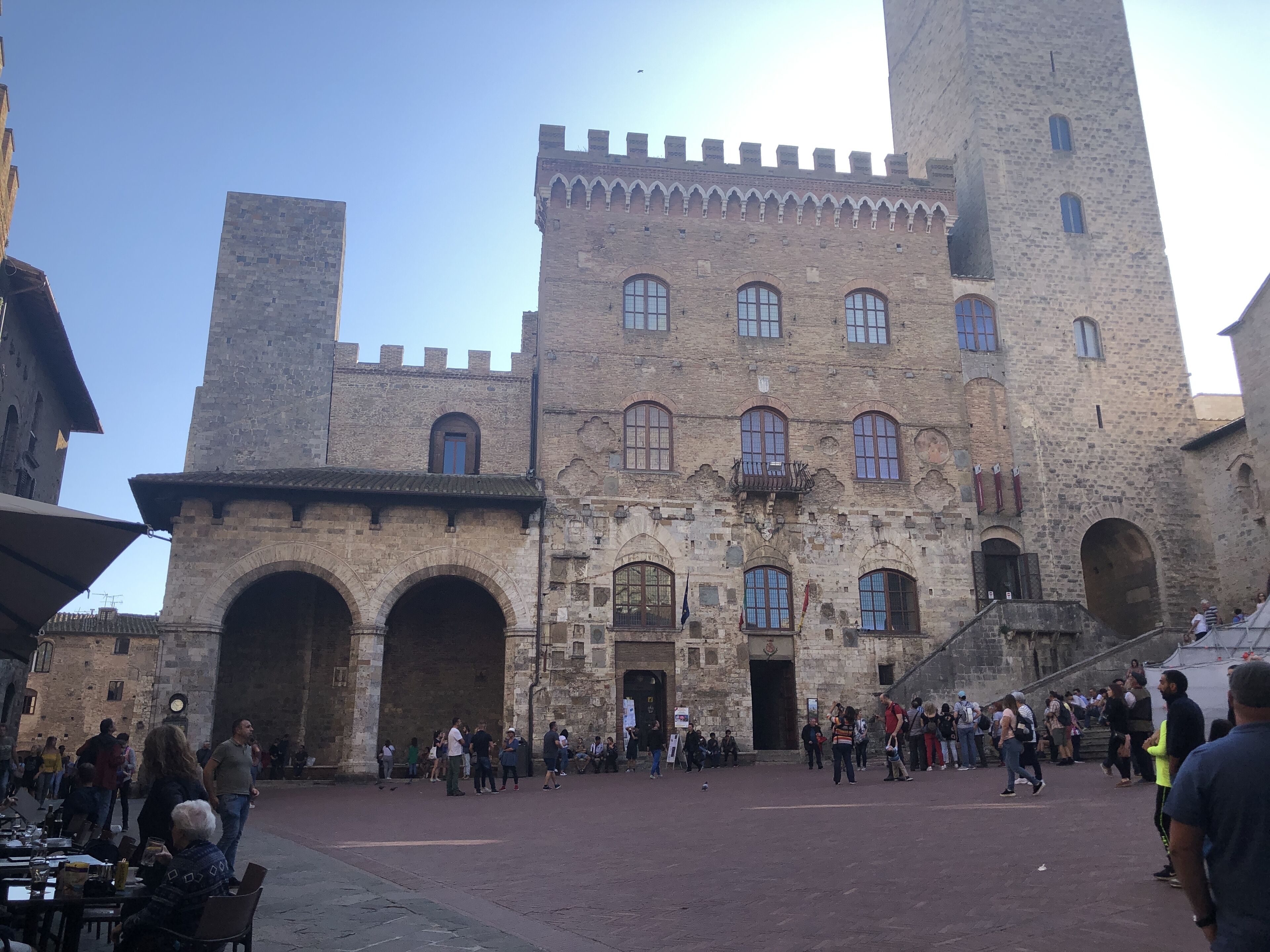 Un bâtiment historique doté d’arcades et d’une entrée centrale, entouré d’une cour où se trouvent des personnes.