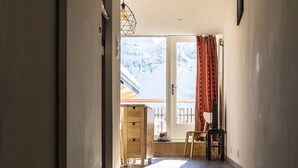 Ein Flur mit Holzboden, einem Holztisch, einem Stuhl, einer Pendelleuchte und einem Fenster mit Blick auf schneebedeckte Berge.