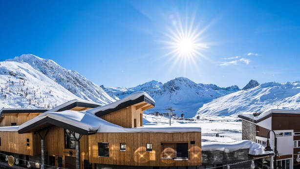Ein modernes Holzgebäude mit einer Seilbahn im Hintergrund, umgeben von schneebedeckten Bergen.