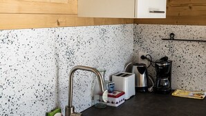 Eine Küche mit einer Spüle aus Edelstahl, einer Kaffeemaschine, einem Toaster und einem Wasserkocher auf der Arbeitsfläche.