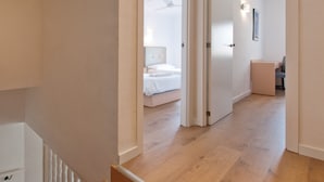 Un couloir au plancher de bois mène à une chambre à coucher qui contient un lit et une table de chevet.