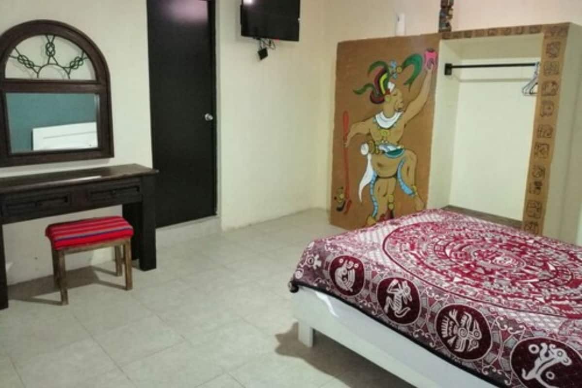Un dormitorio con cama, escritorio, silla, televisor y una puerta.