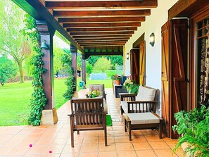 Eine überdachte Terrasse mit Holzmöbeln und Blumentöpfen, mit Blick auf eine Rasenfläche.