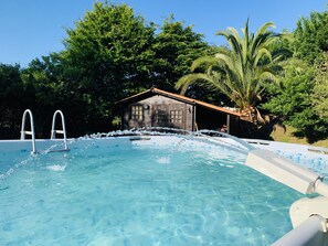 Ein Schwimmbecken mit klarem, blauem Wasser, umgeben von üppiger Vegetation und einer Holzhütte.