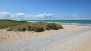 Eine Küstenstraße führt zu einem Strand mit Dünen und blauem Himmel.