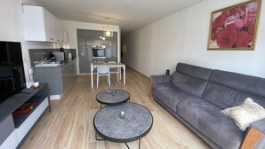 Ein modernes Wohnzimmer mit einem grauen Sofa, zwei runden Tischen, einem Fernseher und einer Küche im Hintergrund.