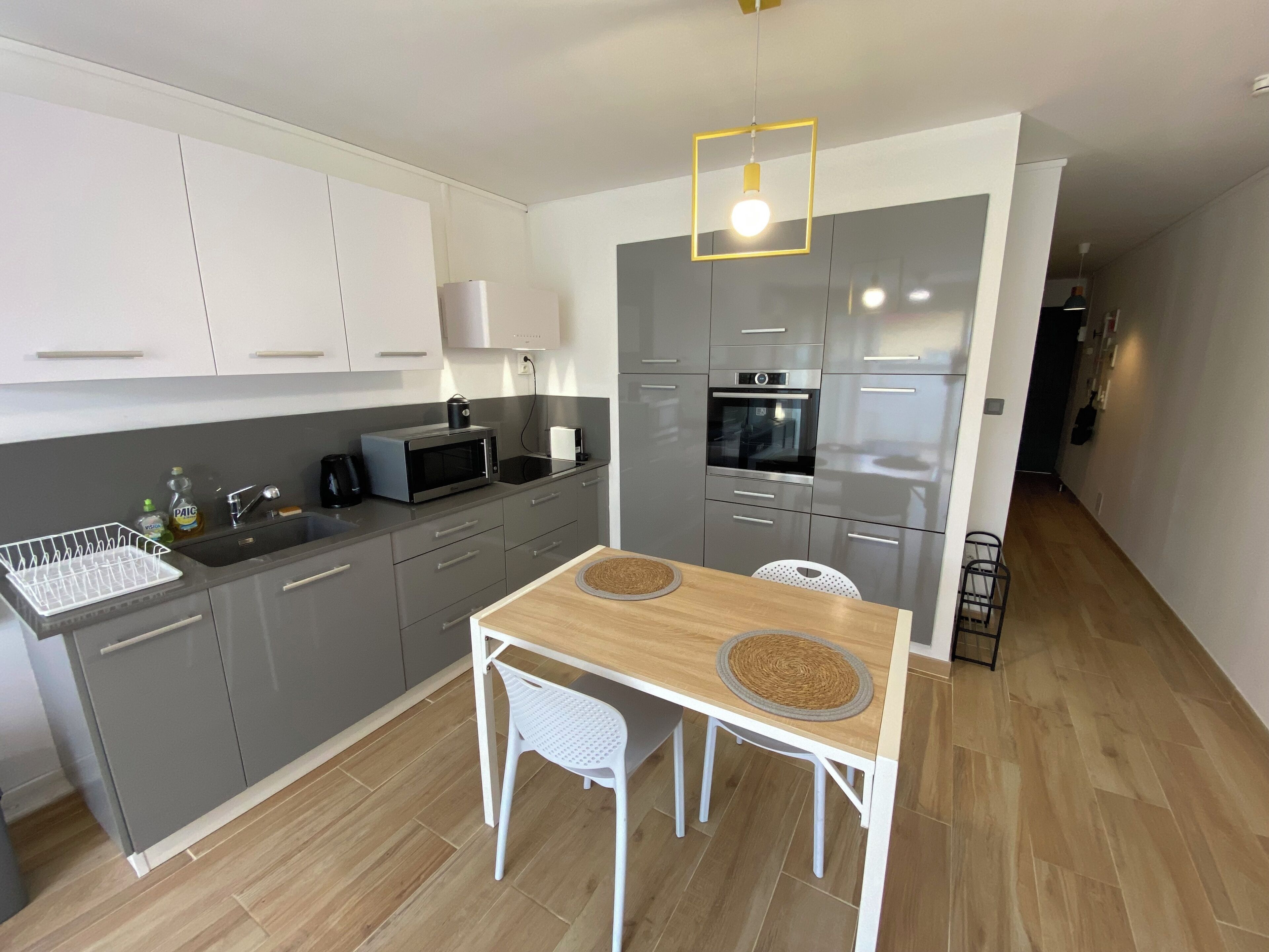 Une cuisine moderne avec des meubles gris, un four à micro-ondes, un four traditionnel et une table à manger avec deux chaises.